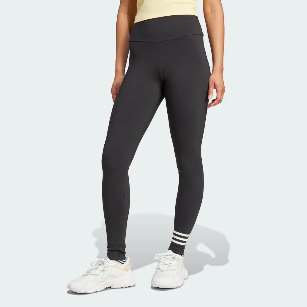 Front three-quarter view of a model wearing the black adidas Neuclassics leggings paired with white trainers, showing the high-waisted fit, full-length leg coverage, and three horizontal white stripes wrapping around the left lower shin.