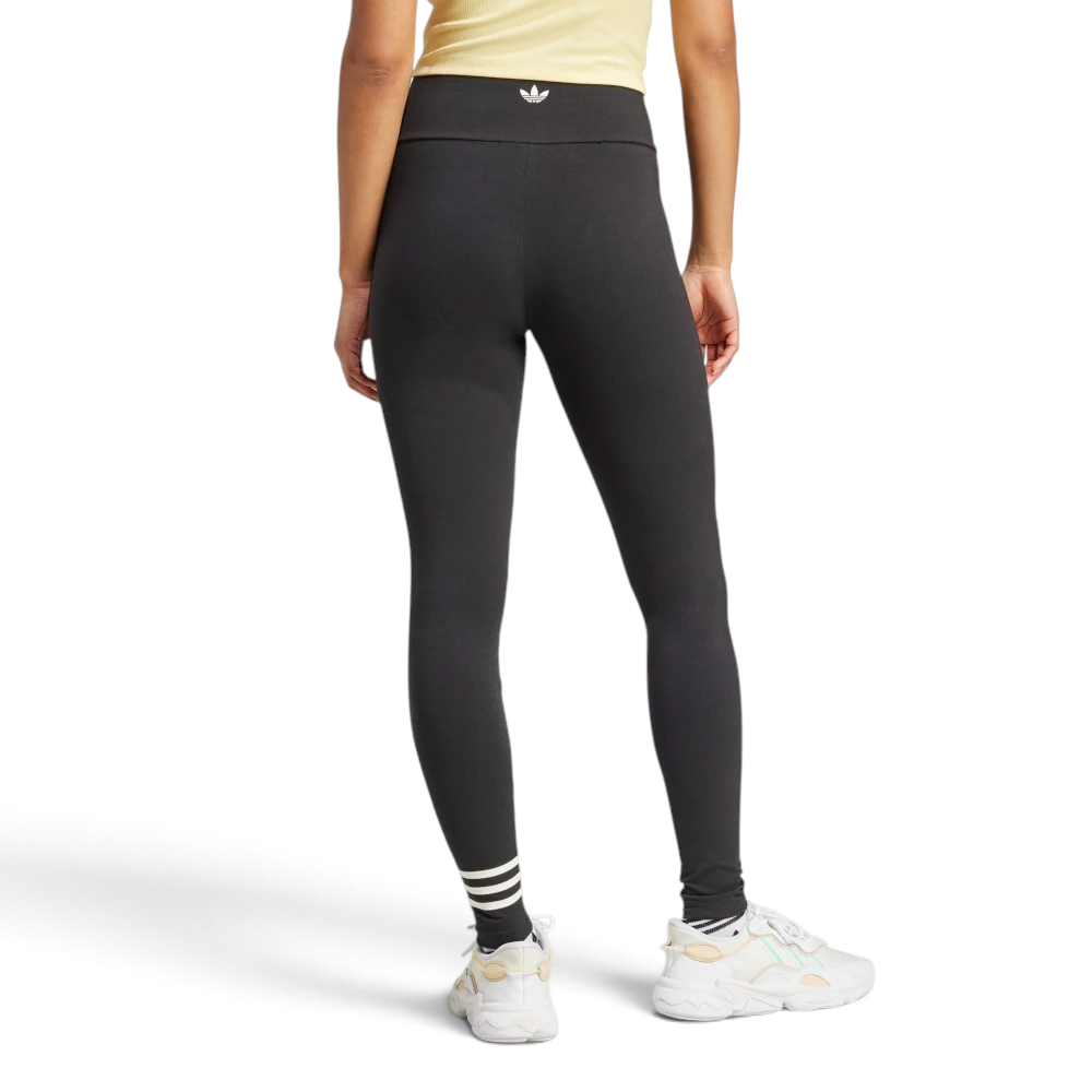 Rear view of the model wearing the black high-waisted adidas Neuclassics leggings, highlighting the small white adidas Trefoil logo printed on the back of the waistband and the asymmetric three white stripes around the left ankle.