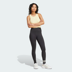 Full-length front view of the model standing with arms crossed, wearing a pastel yellow ribbed vest top, the black high-waisted adidas Neuclassics leggings, and chunky white trainers.