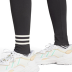 Detailed close-up view of the lower legs and white trainers, highlighting the three contrasting white horizontal 3-Stripes wrapped around the left shin of the black leggings.