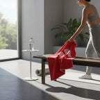 Person in workout attire holding a red towel in a modern room with a table and plant.