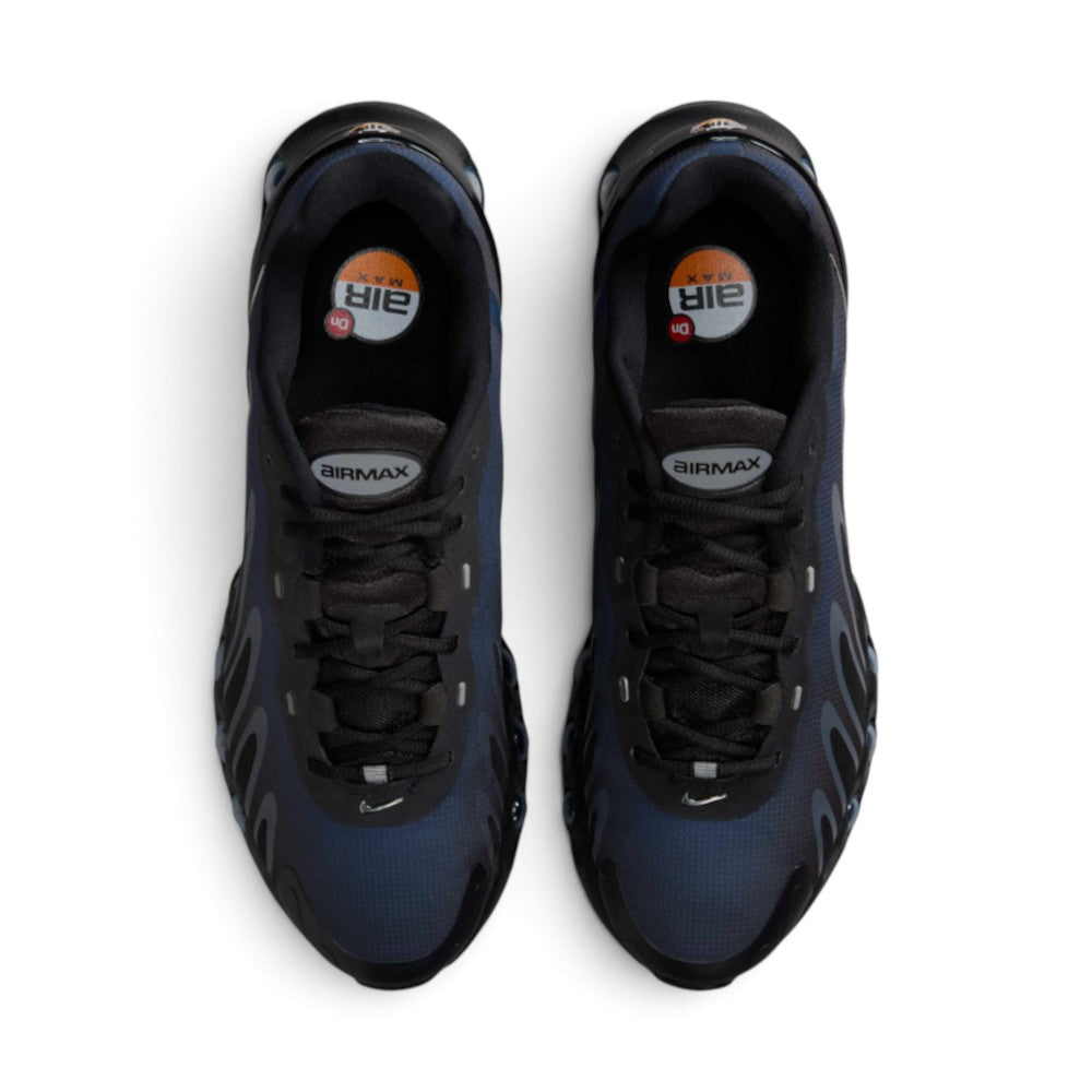 Focuses on the locked-in central lacing layout, displaying flat black laces, black mesh tongues topped with oval metallic "AIRMAX" badges, reflective lace loop accents, and black insoles printed with circular orange-and-white Air Max branding.