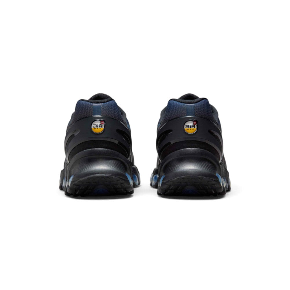 Focuses on the rear profile, displaying the contoured black plastic heel clips, circular yellow-and-white "Air Max Dn" heel badges, blue gradient collar mesh, and the flared base of the rubber outsole.