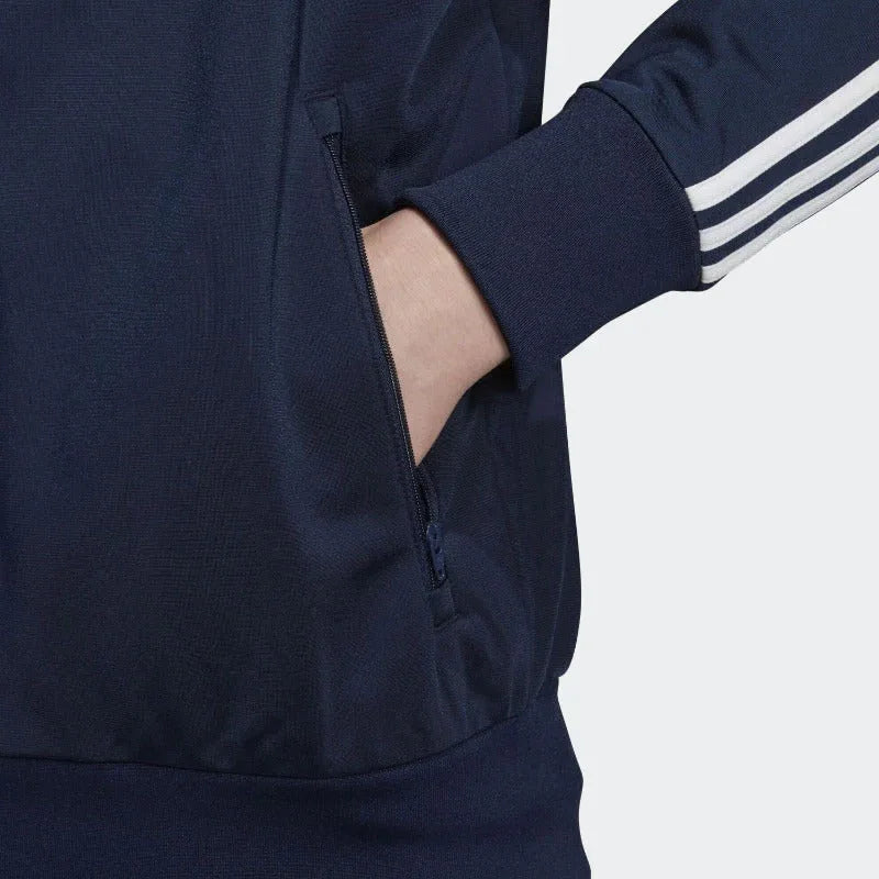 Close-up zoom on the Adidas Firebird Track Jacket Men's, showing the smooth tricot fabric texture and the 3 stripes on the arm with hand in pocket
