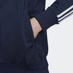 Close-up zoom on the Adidas Firebird Track Jacket Men's, showing the smooth tricot fabric texture and the 3 stripes on the arm with hand in pocket