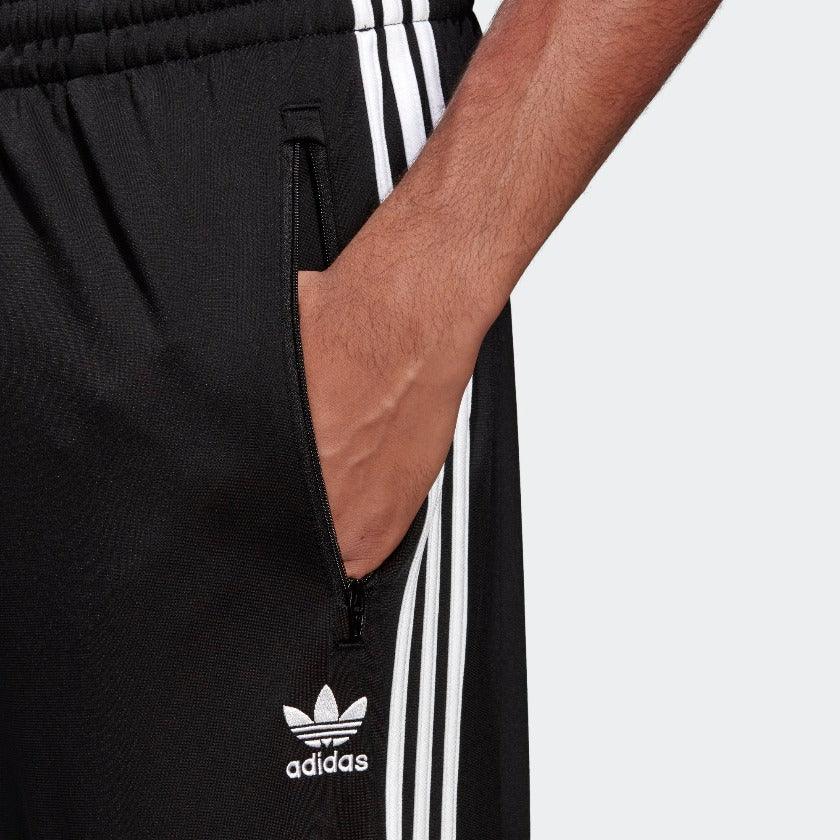 Close-up zoom on the Adidas Firebird Track Pants Men's in black, showing the smooth tricot fabric texture and the embroidered white Trefoil logo detail.